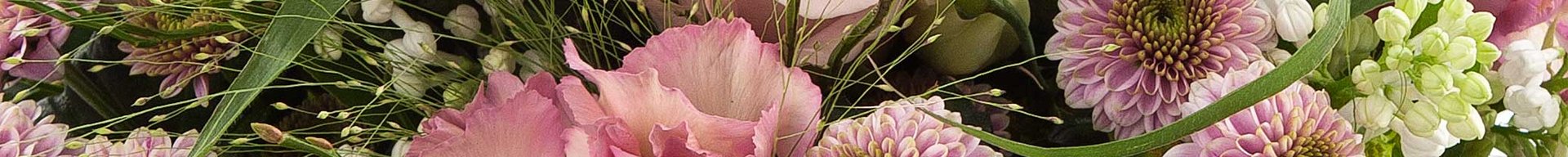 Et farverigt blomsterarrangement med lyserøde roser, dahliaer og nelliker. Arrangementet indeholder også grønne blade og mindre hvide blomster, hvilket skaber et frodigt og livligt udtryk.